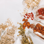 A tabletop view of an array of glass jars with nuts spilled on a white table